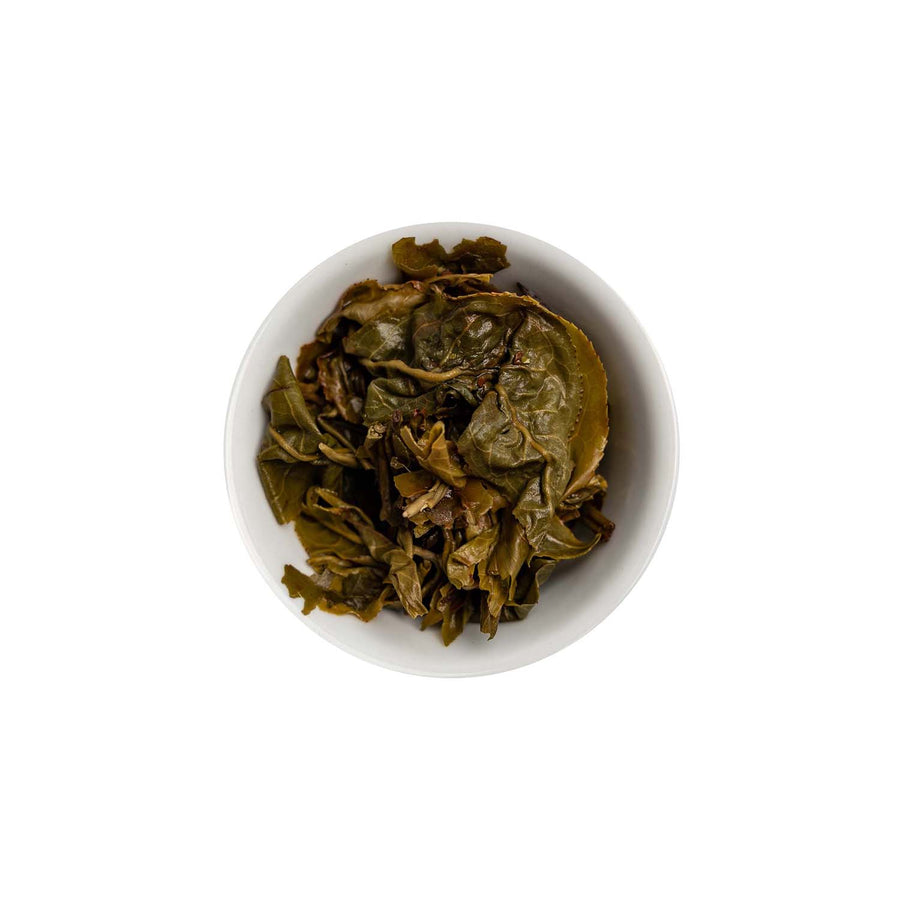 Ein ansprechendes Foto von den losen, aufgebrühten Blättern unseres Grünen Tees Curly Green in einer Tasse.